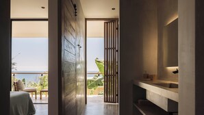 Een moderne badkamer met een grote spiegel, een wastafelblad en uitzicht op de oceaan door een schuifdeur.