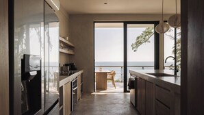 Een moderne keuken met uitzicht op zee, een eethoek met tafel en stoelen, en een grote schuifdeur naar buiten.