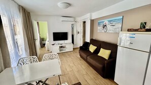 A modern living room with a flat-screen TV, a brown sofa with yellow cushions, a white dining table, and a refrigerator. - Casa Del Mar Apartment in the Old Town of Benidorm (Benidorm)
