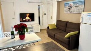 A modern living room with a flat-screen TV, a brown sofa, a white table with a red flower vase, and a white refrigerator. - Casa Del Mar Apartment in the Old Town of Benidorm (Benidorm)