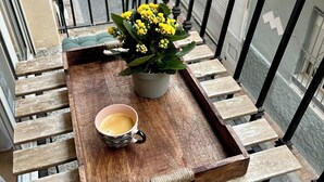 A balcony with a wooden bench, a potted plant with yellow flowers, and a tray with a cup of coffee. - Casa Del Mar Apartment in the Old Town of Benidorm (Benidorm)