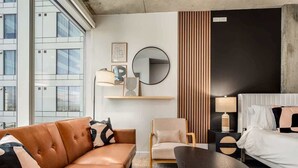 A modern hotel room with a leather sofa, a round table, a bed with white bedding, a round mirror, and a wooden panel wall. - Boulevard Stays Downtown Highrise STU Sky Pool, Parking, Gym 03 (Phoenix)