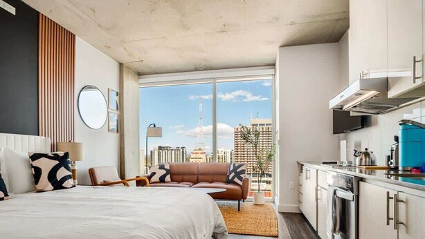 A modern bedroom with a large bed, a sofa, and a view of the city skyline through large windows. - Boulevard Stays Downtown Highrise STU Sky Pool, Parking, Gym 06 (Phoenix)