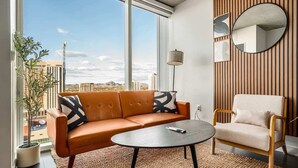 A modern living room with a sofa, armchair, and coffee table, large windows with a city view, and a wooden wall panel. - Boulevard Stays Downtown Highrise STU Sky Pool, Parking, Gym 07 (Phoenix)
