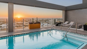 A rooftop pool with a city view at sunset, lounge chairs, and a planter with plants. - Boulevard Stays Downtown Highrise STU Sky Pool, Parking, Gym 09 (Phoenix)