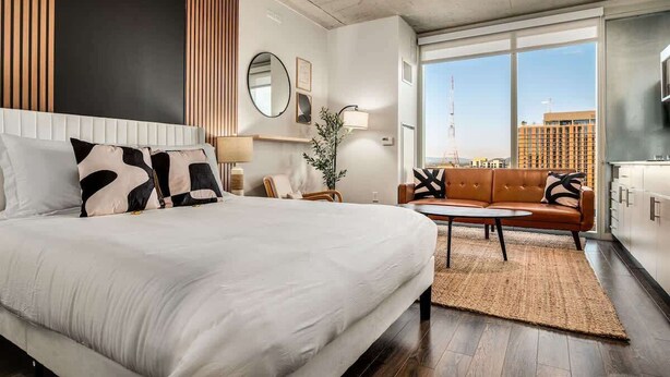 A modern hotel room with a large bed, a sofa, a small table, and a view of the city through large windows. - Boulevard Stays Downtown Highrise STU Sky Pool, Parking, Gym 09 (Phoenix)