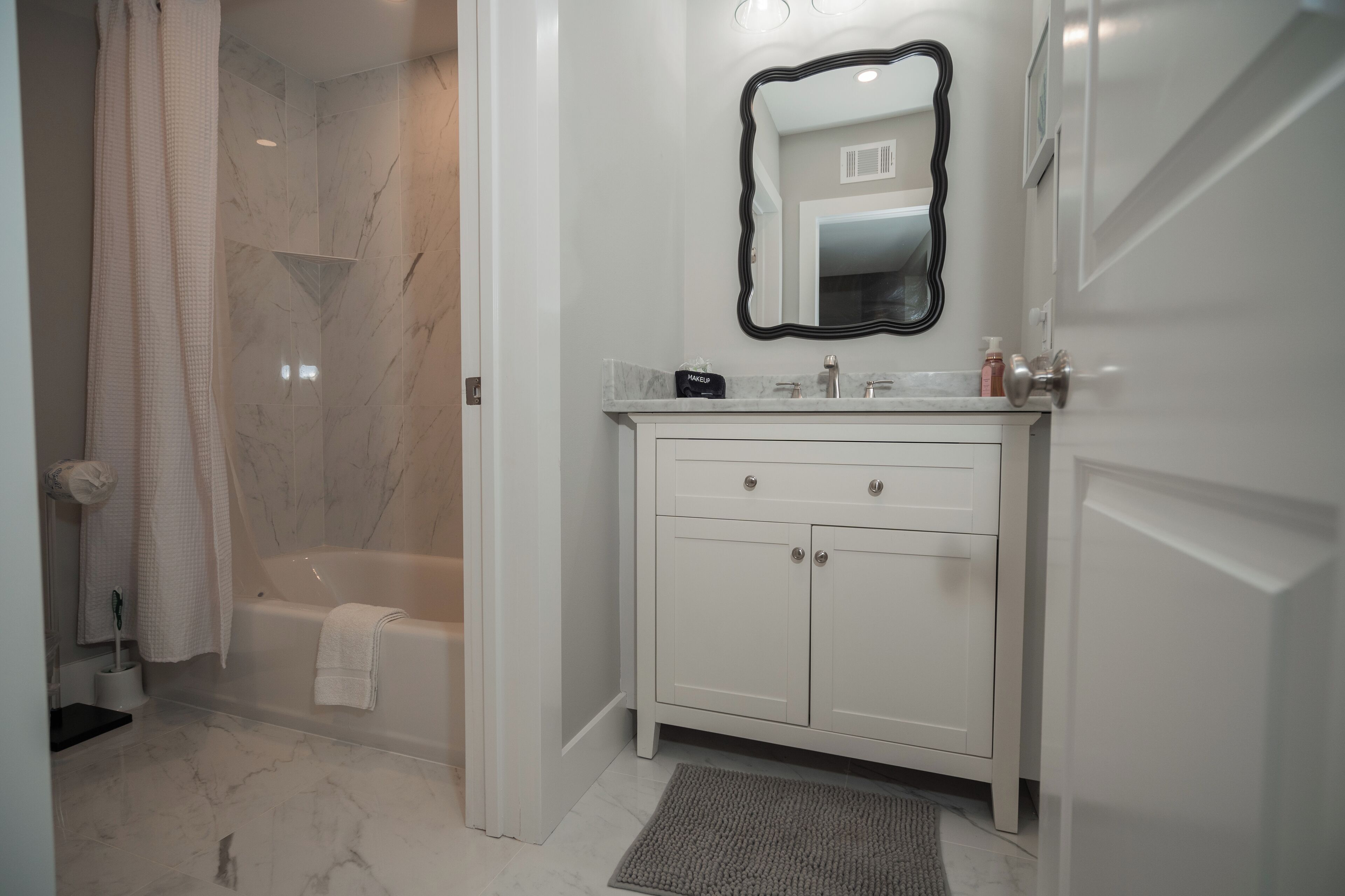 A bathroom with a bathtub, a white vanity with a mirror, and a shower curtain.
