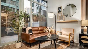 A modern living room with a leather sofa, a round coffee table, a side chair, a large window, and a mirror on the wall.