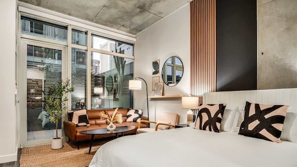 A modern hotel room with a large bed, a sofa, a coffee table, and a potted plant.