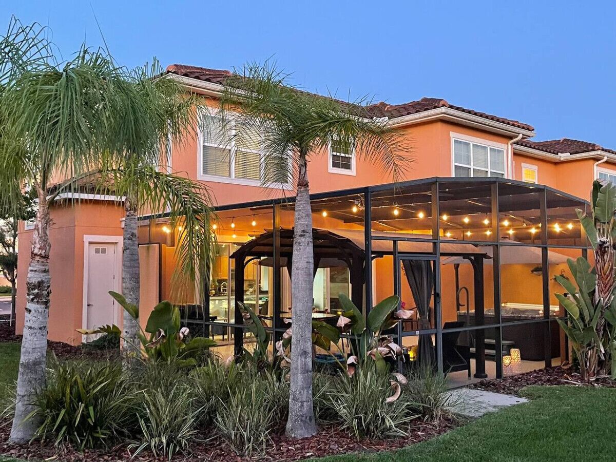 A house with a covered outdoor seating area, surrounded by palm trees and tropical plants.