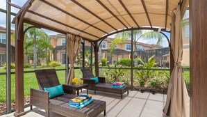 Un patio couvert aménagé avec des meubles en osier, des coussins et une table sur laquelle se trouve une boisson.