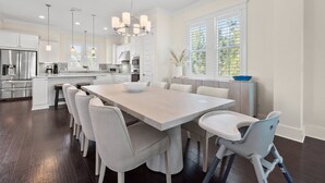Een moderne keuken met een groot eiland, witte kasten, en een eethoek met een lange tafel en stoelen.