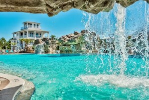 Une piscine à l’eau turquoise et limpide, une cascade et, au fond, un immeuble à plusieurs étages.