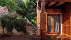 Um deck de madeira que leva a uma escadaria de pedra, com uma porta e portadas de madeira.