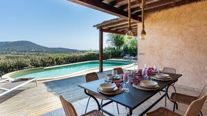 Uma área de refeições com vista para a piscina, deck de madeira e mobiliário para áreas externas.