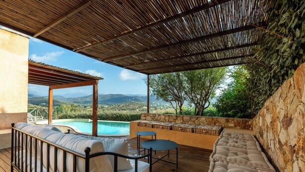 Uma área de estar coberta ao ar livre com vista para uma piscina e montanhas.