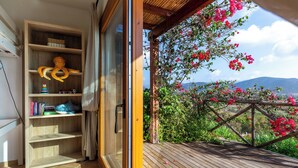 Estante de madeira com livros e um brinquedo de polvo macio, uma porta de vidro deslizante que dá para um deck de madeira com vista para um jardim e montanhas.