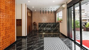 A hotel reception area with a check-in counter, a patterned wall, and a red carpet leading to the entrance. - Aurea Delight Hotel (Phnom Penh)
