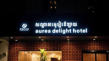 Un letrero de hotel con un logotipo y nombre, fachada decorada y una planta en la entrada.