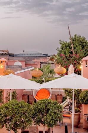 A rooftop terrace with white umbrellas, wicker lanterns, potted plants, and a view of the cityscape. - Riad Luciano Hotel & Spa (Marrakech)