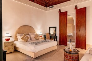 A bedroom with a large bed, bedside tables, a dresser, a mirror, and a bathroom with a sink. - Riad Luciano Hotel & Spa (Marrakech)