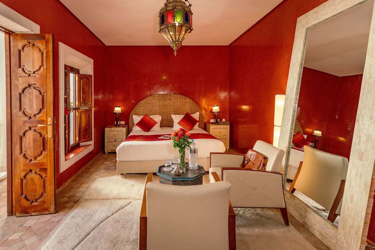 A hotel room with a large bed, two bedside tables, a sitting area with a chair and a small table, and a large mirror.