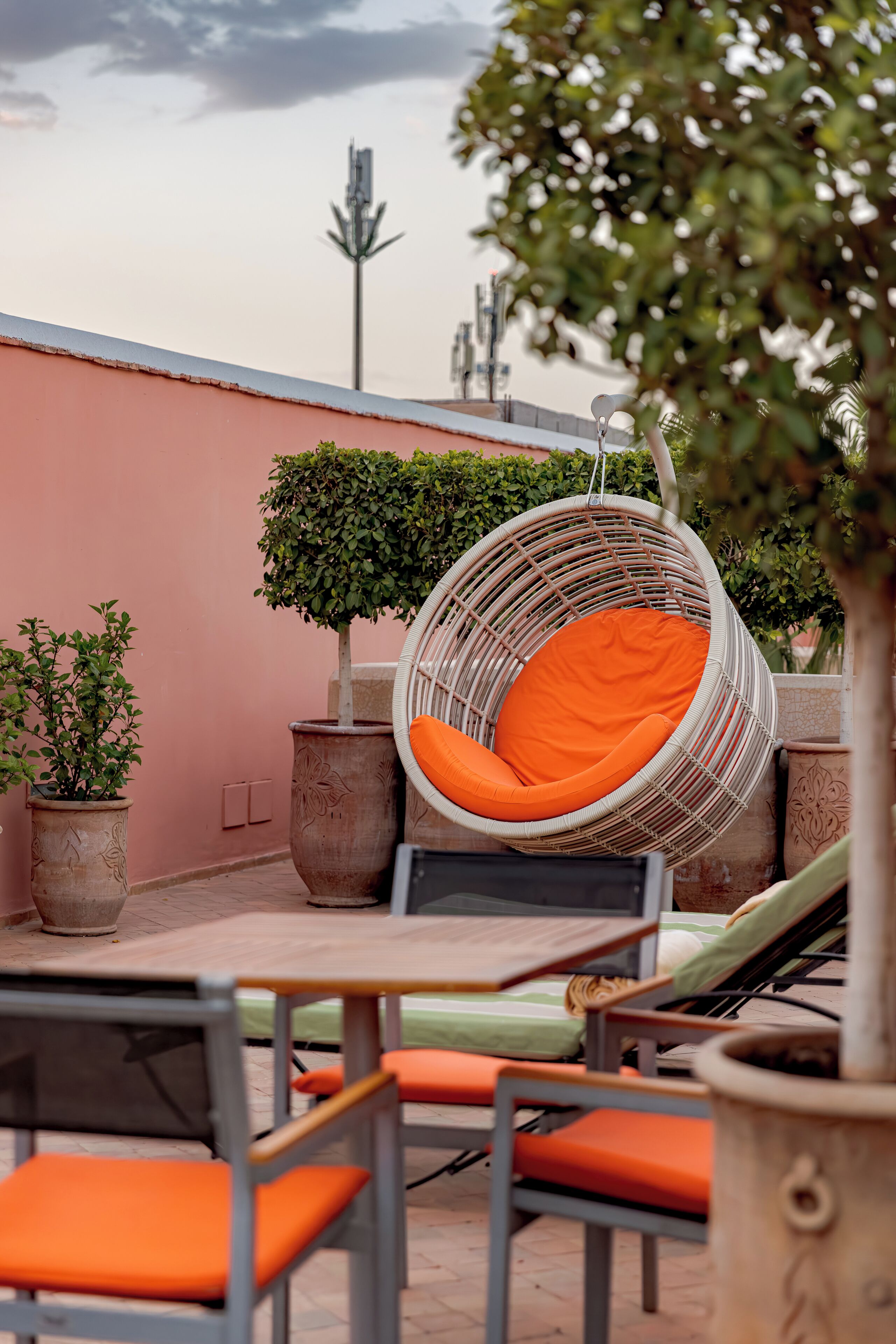 A rooftop terrace with a hanging chair, potted plants, and outdoor seating.