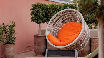 A rooftop terrace with a hanging chair, potted plants, and outdoor seating.