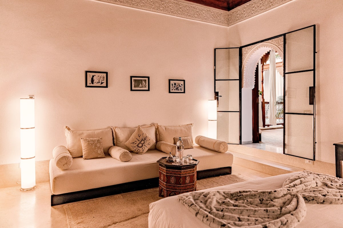 A room with a beige sofa, a small side table, and a bed with a patterned throw.