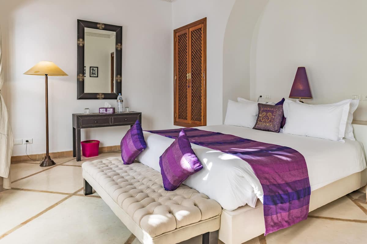 A bedroom with a bed, a bench, a dresser, a mirror, and a wardrobe.