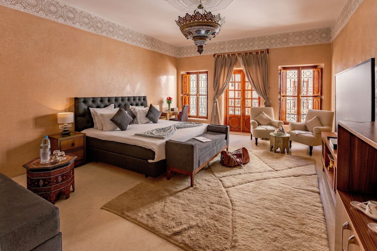 A spacious bedroom with a large bed, a television, a sofa, and a decorative chandelier.