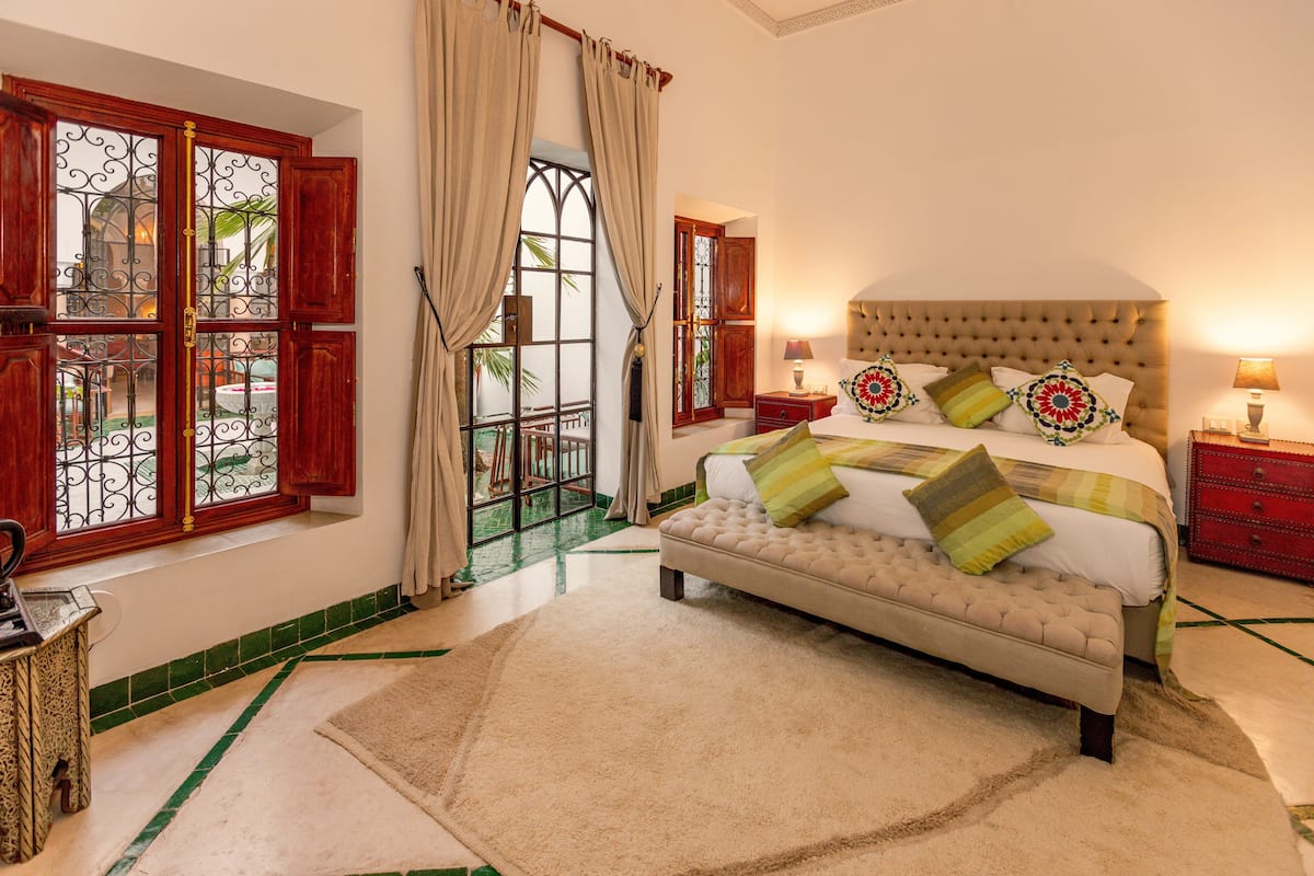 A bedroom with a large bed, a bench, a nightstand, and a window with curtains.