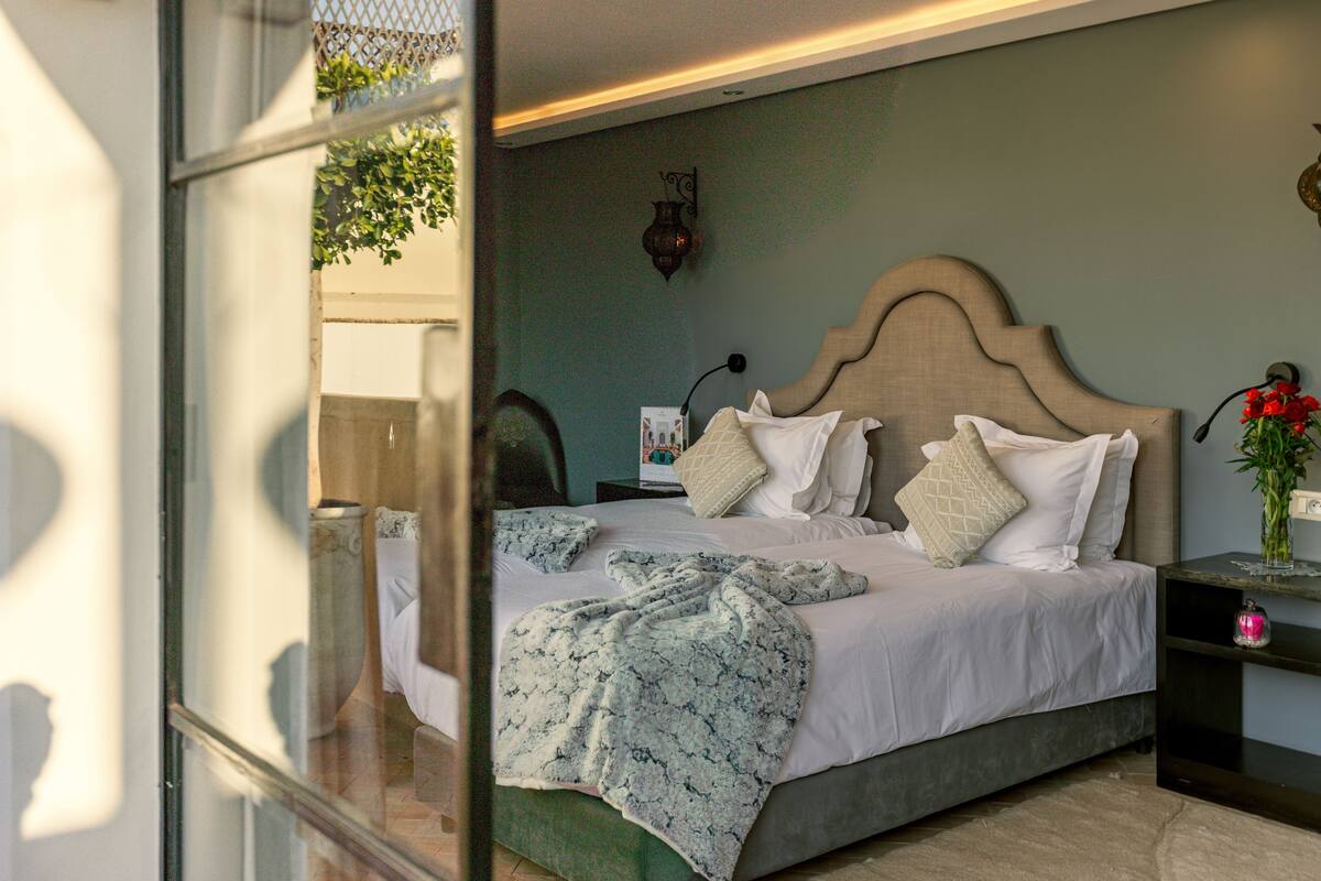 A neatly made bed with a patterned blanket, a bedside table with a vase of flowers, and a wall-mounted lamp.