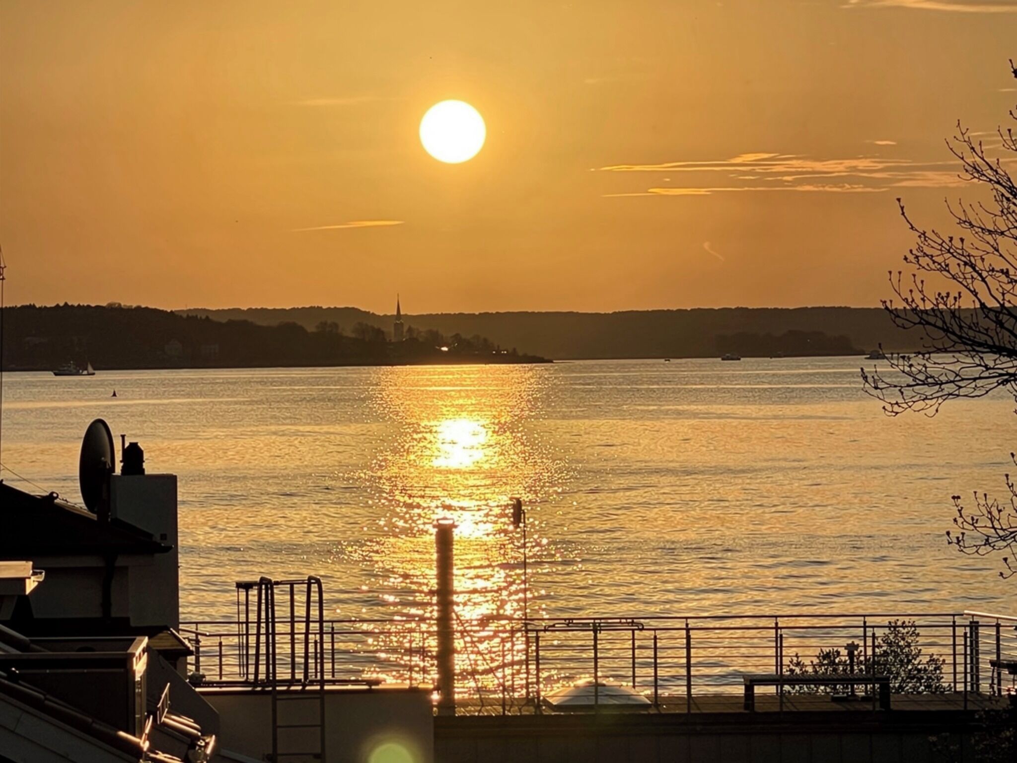Blick auf das Wasser bei Sonnenuntergang, eine Wasseroberfläche und eine ferne Küstenlinie.