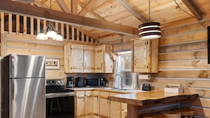 Cocina de cabaña de madera con un refrigerador, microondas y horno de acero inoxidable. Hay taburetes de madera y una barra de madera.