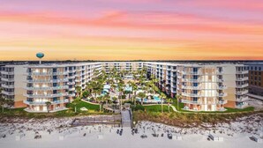 Un resort con varias edificaciones, un área de piscina central y una playa en primer plano.