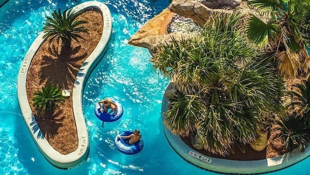 Vista aérea de una piscina con dos jacuzzis y plantas tropicales alrededor.
