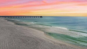 Una playa con un muelle que se adentra en aguas tranquilas bajo un cielo de atardecer colorido.