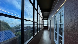 A corridor with large windows, a tiled floor, and a view of a body of water and distant landscape. - W & H View Residency (Kochi)