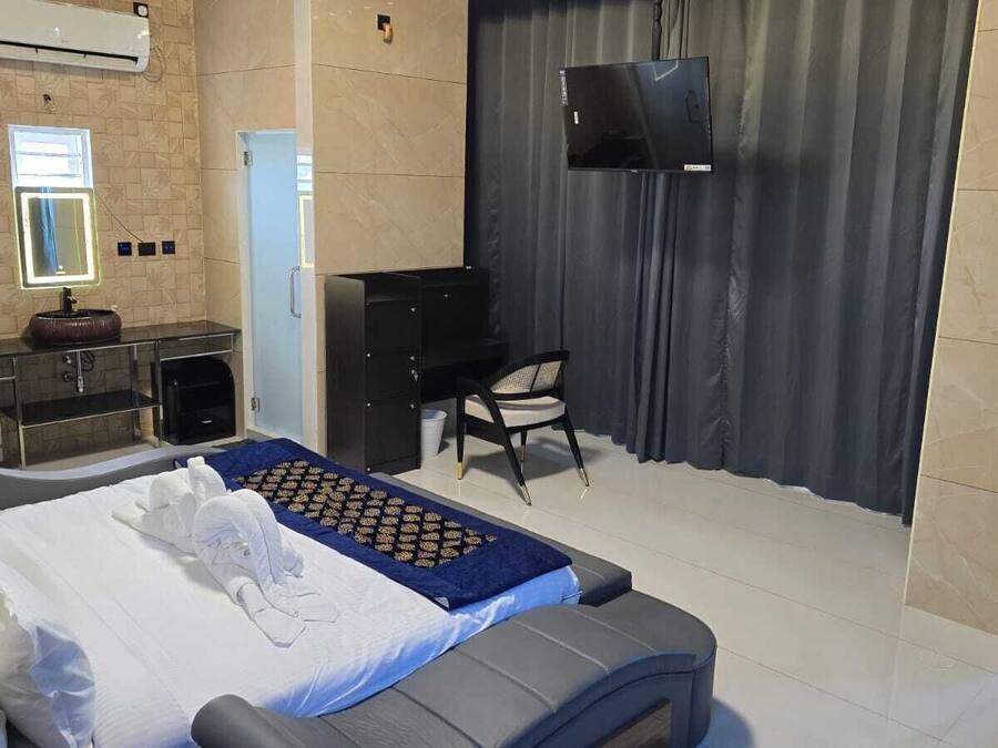 A hotel room with a bed, a desk, a chair, a TV, and a bathroom.