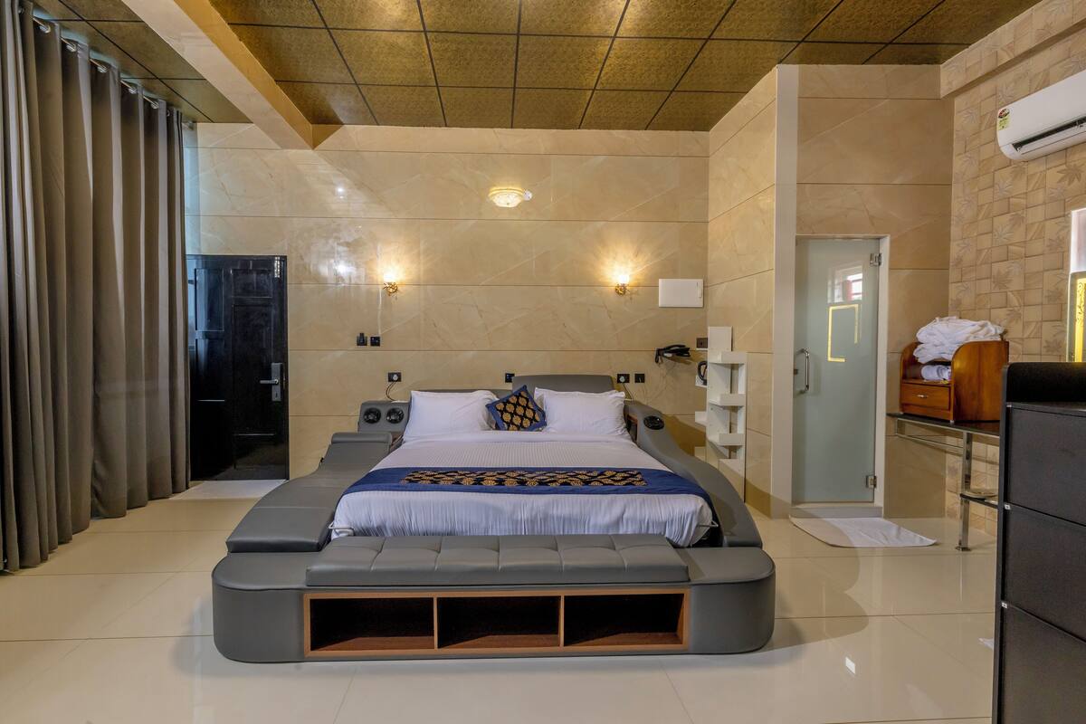 Ein modernes Hotelzimmer mit einem großen Bett, einer integrierten Sitzbank, einem begehbaren Kleiderschrank und einem Badezimmer mit Glastür.
