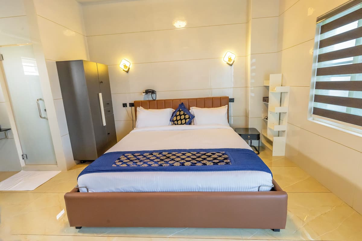 Ein modernes Hotelzimmer mit einem großen Bett, einem Schrank, einem Schreibtisch und einem Fenster mit Jalousien.