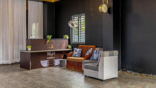 A reception area with a wooden desk, a sofa, and a clock on the wall. - W & H View Residency (Kochi)