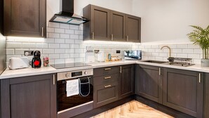 A modern kitchen with dark wooden cabinets, a stainless steel range hood, and a white tiled backsplash. - InspoHome Bayview 1-Bed Cardiff Bay  (Cardiff)