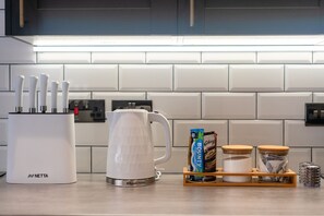Una cucina con mobili bianchi, un bollitore, un portachiodi e alcuni snack confezionati.