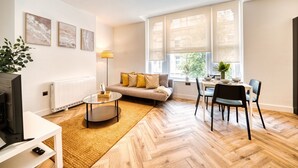 A modern living room with a sofa, coffee table, and dining area. - InspoHome Bayview 1-Bed Cardiff Bay  (Cardiff)