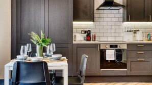 A modern kitchen with dark wood cabinets, a built-in oven, and a coffee machine. - InspoHome Bayview 1-Bed Cardiff Bay  (Cardiff)