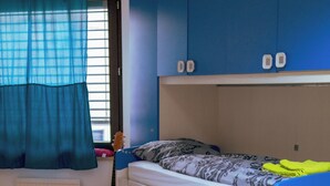 Une chambre avec deux lits superposés, une fenêtre avec des rideaux et une guitare appuyée contre le mur.