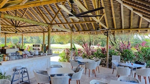 Um pátio coberto ao ar livre com mesas e cadeiras, área de bar e vista para um campo de golfe.