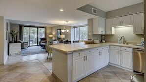 A modern kitchen with white cabinets, a large island, and a dining area with a view to the outdoors.